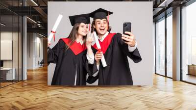 Male and female student taking a selfie with mobile phone on white background Wall mural